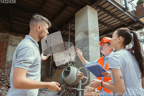 Image of Foreman or achitect shows house, office or store design plans to a young couple