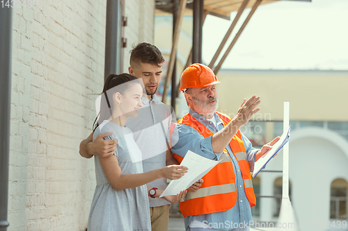 Image of Foreman or achitect shows house, office or store design plans to a young couple