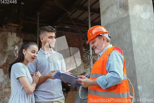 Image of Foreman or achitect shows house, office or store design plans to a young couple