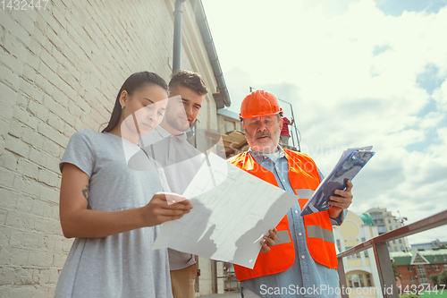 Image of Foreman or achitect shows house, office or store design plans to a young couple