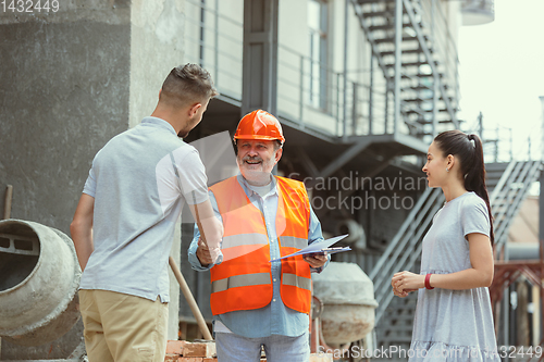 Image of Foreman or achitect shows house, office or store design plans to a young couple