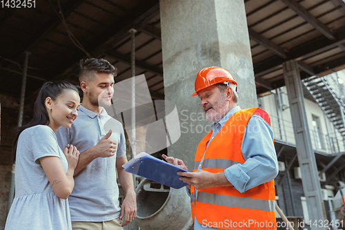 Image of Foreman or achitect shows house, office or store design plans to a young couple