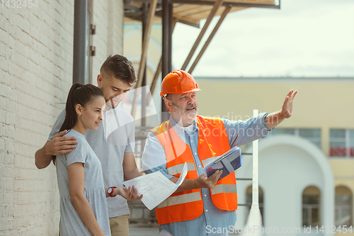 Image of Foreman or achitect shows house, office or store design plans to a young couple