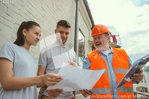 Image of Foreman or achitect shows house, office or store design plans to a young couple