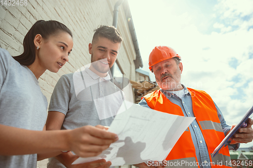 Image of Foreman or achitect shows house, office or store design plans to a young couple