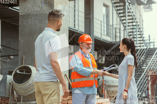 Image of Foreman or achitect shows house, office or store design plans to a young couple