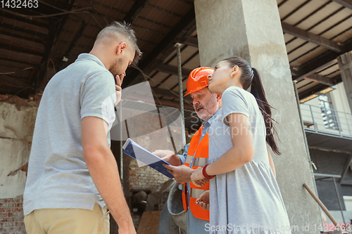 Image of Foreman or achitect shows house, office or store design plans to a young couple