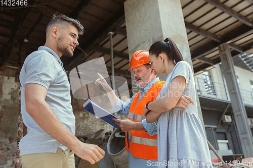 Image of Foreman or achitect shows house, office or store design plans to a young couple