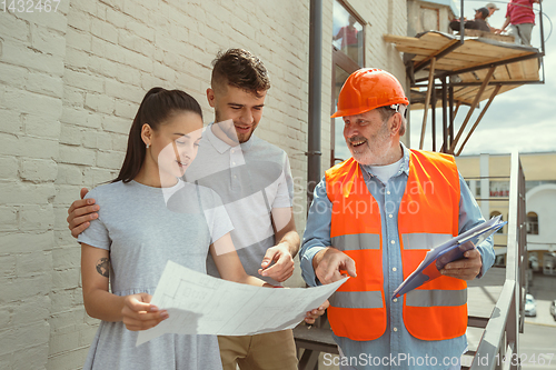 Image of Foreman or achitect shows house, office or store design plans to a young couple