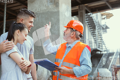 Image of Foreman or achitect shows house, office or store design plans to a young couple