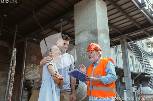 Image of Foreman or achitect shows house, office or store design plans to a young couple