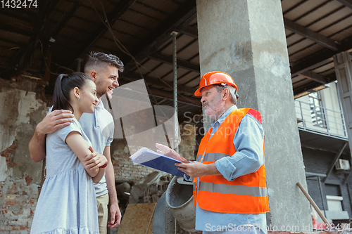 Image of Foreman or achitect shows house, office or store design plans to a young couple