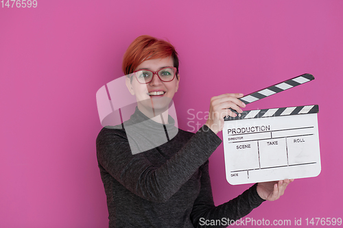 Image of redhead woman holding movie  clapper on pink background