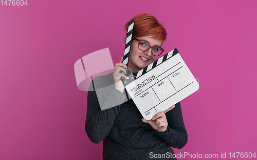 Image of redhead woman holding movie  clapper on pink background