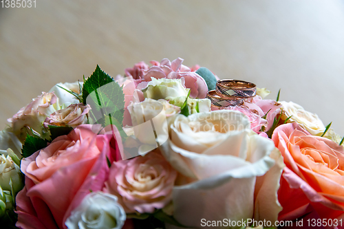 Image of Bouquet of bride with roses and gold wedding rings.