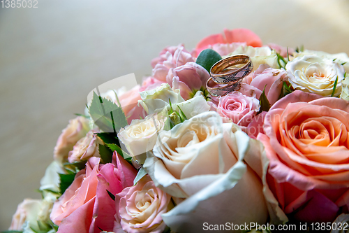 Image of Bouquet of bride with roses and gold wedding rings.