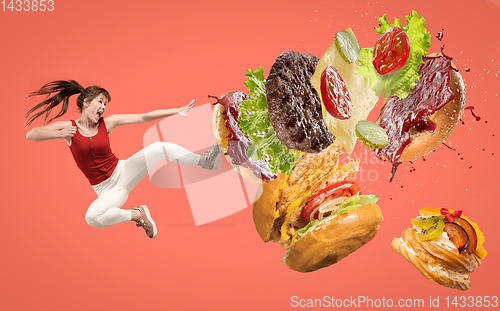 Image of Fast food concept. Young woman fight with burger on red background