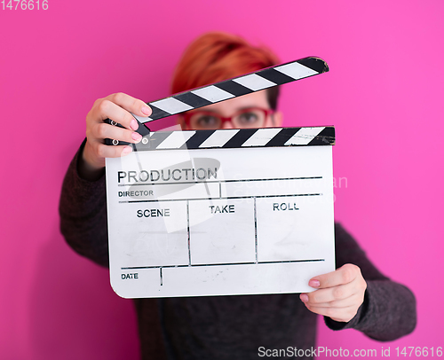 Image of redhead woman holding movie  clapper on pink background