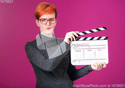 Image of redhead woman holding movie  clapper on pink background