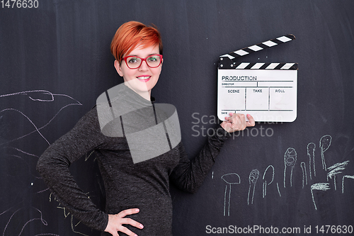 Image of redhead woman holding clapper on black background