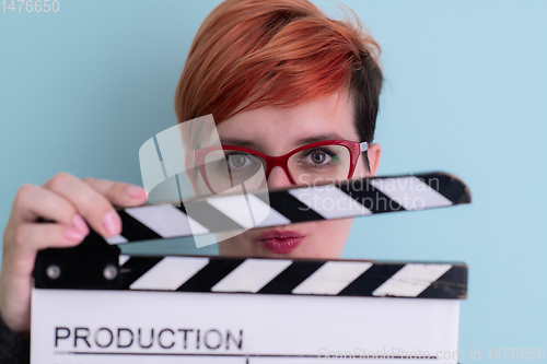 Image of redhead woman holding movie  clapper on cyan background