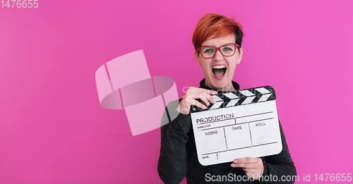 Image of redhead woman holding movie  clapper on pink background