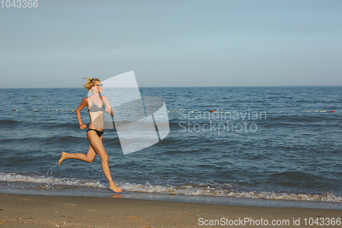 Image of Side view of a woman running on the beach with the horizon and sea in the background