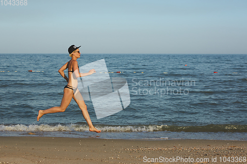 Image of Active sporty woman run along ocean surf by water pool to keep fit and health. Sunset black sand beach background with sun. Woman fitness, jogging workout and sport activity on summer family holiday.