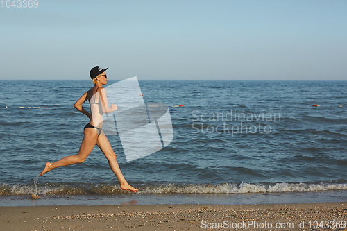 Image of Active sporty woman run along ocean surf by water pool to keep fit and health. Sunset black sand beach background with sun. Woman fitness, jogging workout and sport activity on summer family holiday.