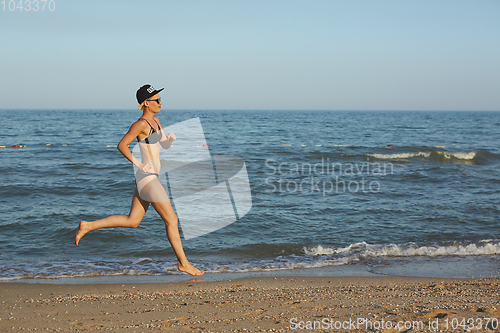 Image of Active sporty woman run along ocean surf by water pool to keep fit and health. Sunset black sand beach background with sun. Woman fitness, jogging workout and sport activity on summer family holiday.