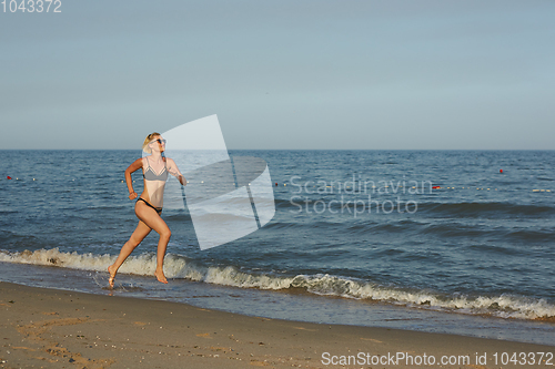 Image of Side view of a woman running on the beach with the horizon and sea in the background