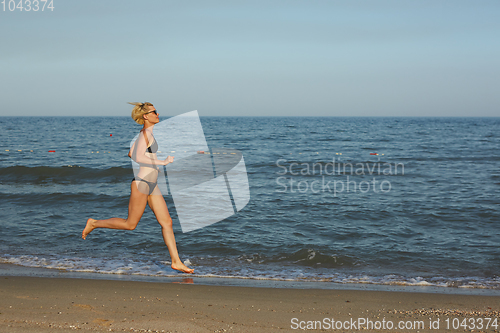 Image of Side view of a woman running on the beach with the horizon and sea in the background