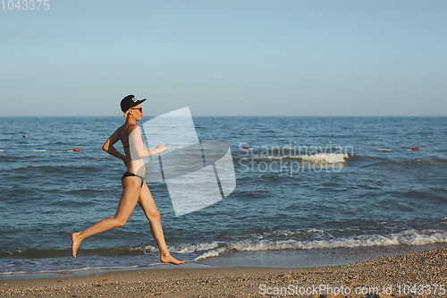 Image of Sexy and happy beautiful woman in bikini running on the beach. In a cap with the inscription queen. Film effect.