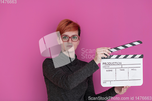 Image of redhead woman holding movie  clapper on pink background