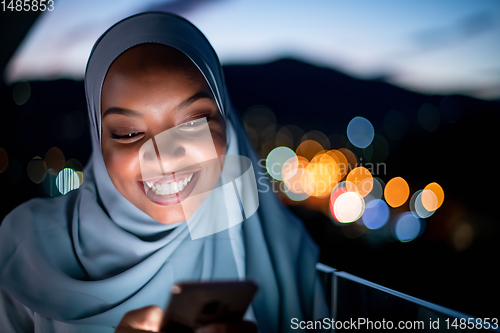 Image of Young Muslim woman on  street at night using phone
