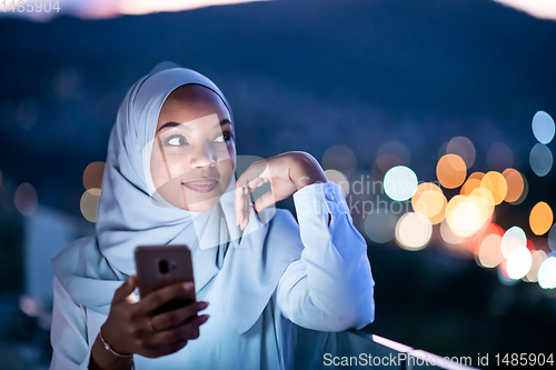 Image of Young Muslim woman on  street at night using phone