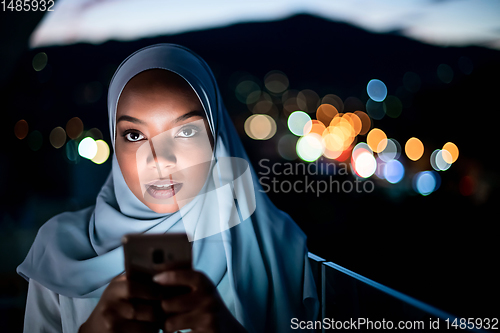 Image of Young Muslim woman on  street at night using phone