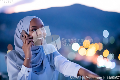 Image of Young Muslim woman on  street at night using phone