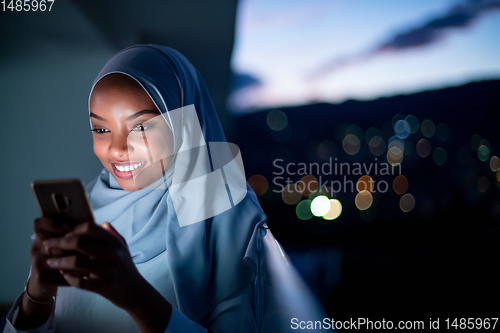 Image of Young Muslim woman on  street at night using phone