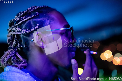 Image of african american man smoking cigarette  at night