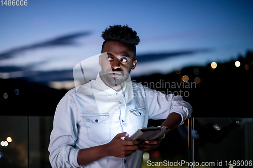 Image of Young  Afro man on street at night using tablet computer