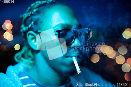 Image of african american man smoking cigarette  at night