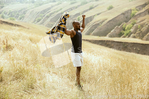 Image of African-american male traveler standing confident at green meadows