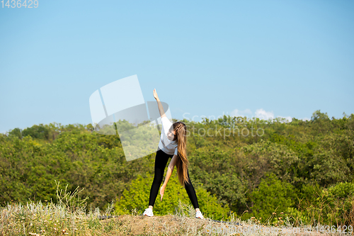 Image of Beautiful young woman training flexibility outdoors