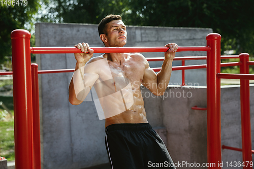 Image of Young muscular man while doing his workout outside at playground