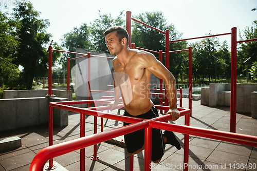 Image of Young muscular man while doing his workout outside at playground