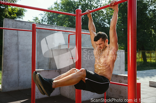 Image of Young muscular man while doing his workout outside at playground