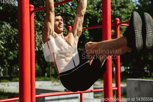 Image of Young muscular man while doing his workout outside at playground