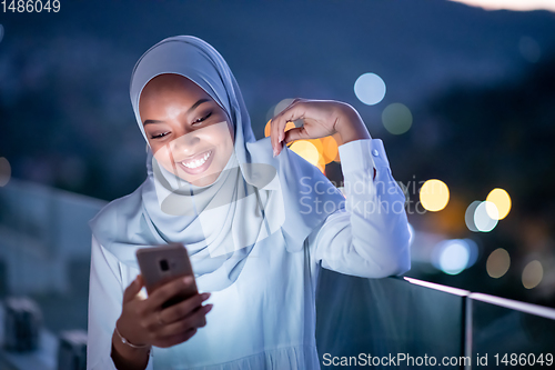 Image of Young Muslim woman on  street at night using phone