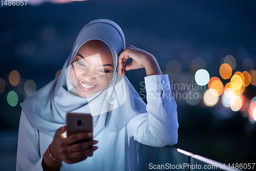 Image of Young Muslim woman on  street at night using phone